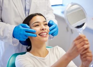 Woman in dentist chair flashes a big smile in the mirror, enjoying her newly whitened teeth after professional cosmetic care removed some extrinsic stains.