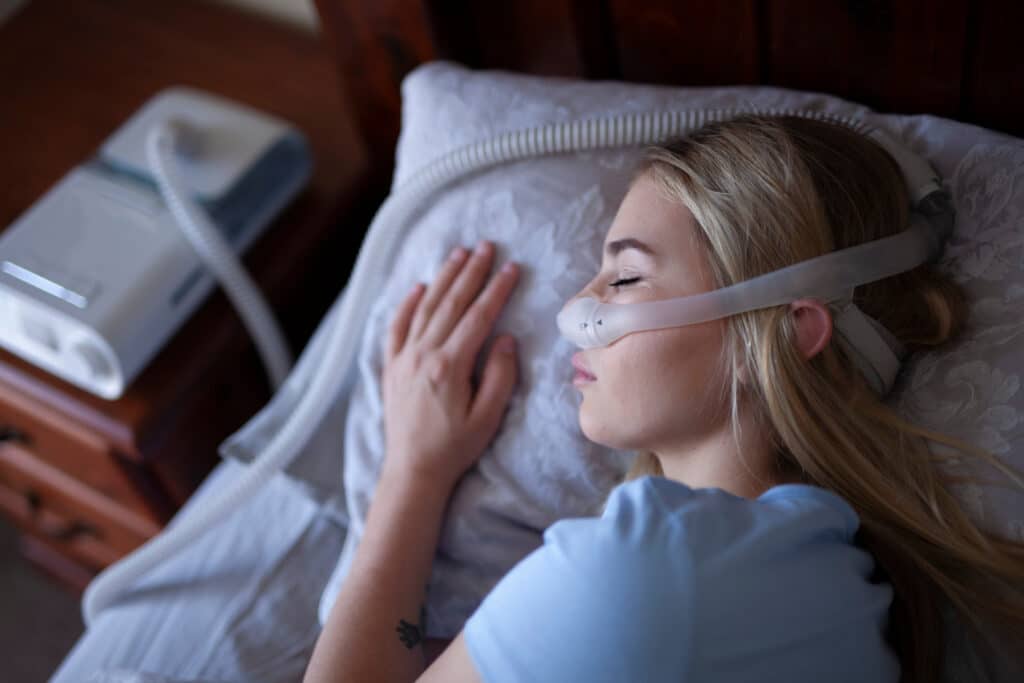 Woman wearing an uncomfortable-looking CPAP machine while sleeping in bed