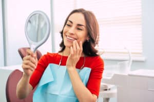 Woman looks in the mirror at her new tooth after receiving a mini dental implant in NYC.