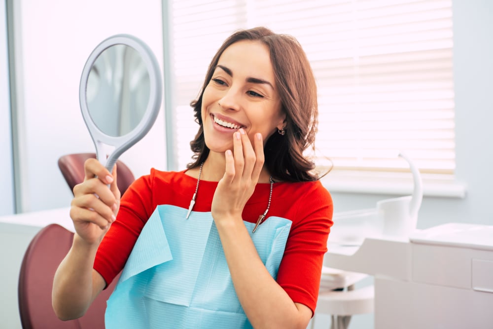 Woman looks in the mirror at her new tooth after receiving a mini dental implant in NYC.