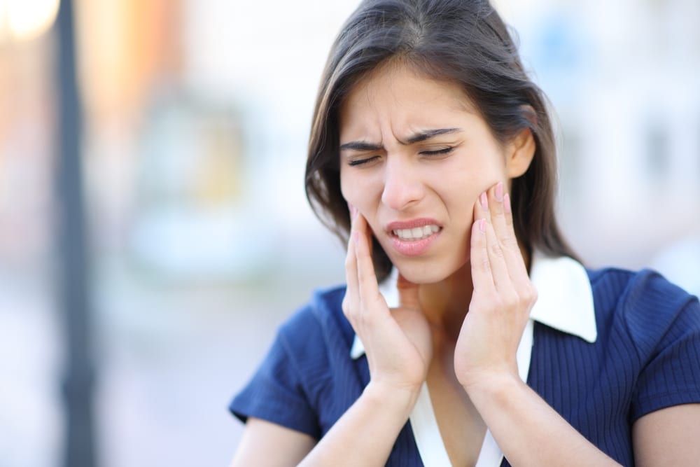NYC woman rubs her face, frustrated by TMJ discomfort.